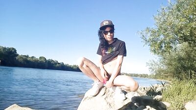 Risky public masturbation, cumshot outside, outdoors, by the water, of a twink with long black hair